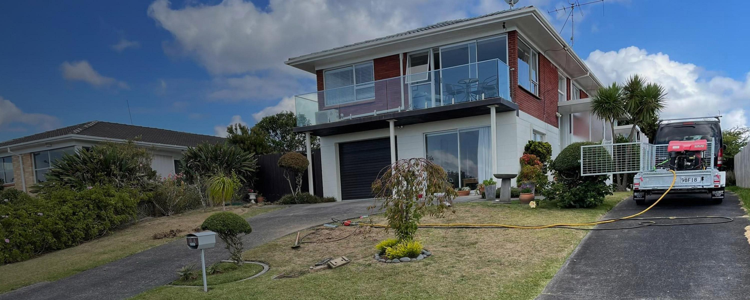A large 2-storey home in Auckland, view of the front lawn with a Leak Solutions truck in their driveway preparing for work on the property | Leak Detection Specialists