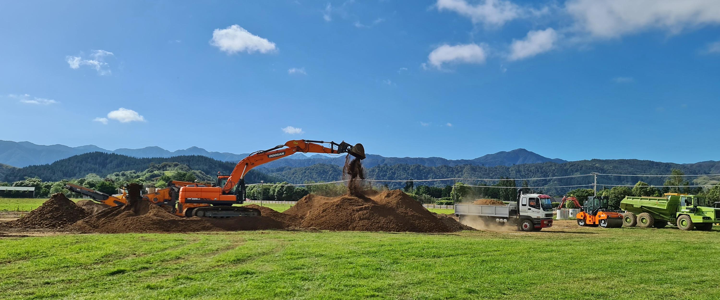 A large Excavator, a roller and two dump trucks on a work site working with a large pile of dirt | Drainage Wellington, Kapiti, Manawatu