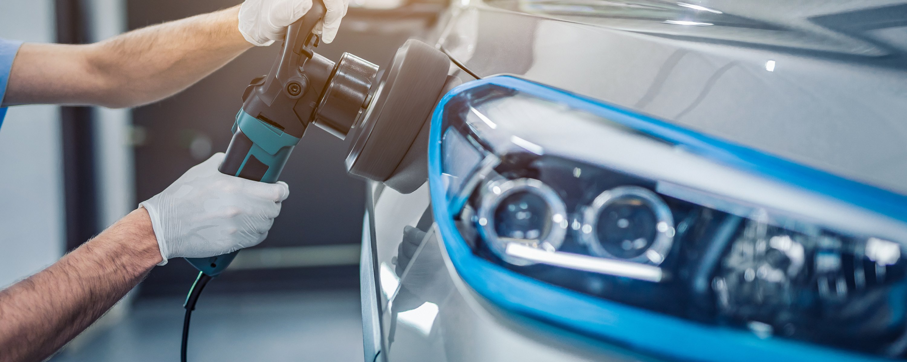 Man with white gloves holding a polishing tool as he makes a dark grey coloured vehicle shine and reflect all the light in the room