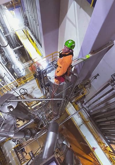 GR Abseiler standing on top of a large dangerous industrial cylinder with his green helmet and orange jumpsuit