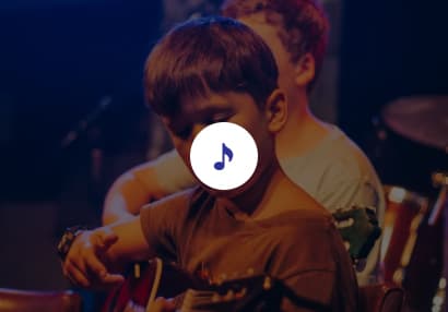 Little boy on stage with colourful lights as he plays the guitar with the rest of the band behind him