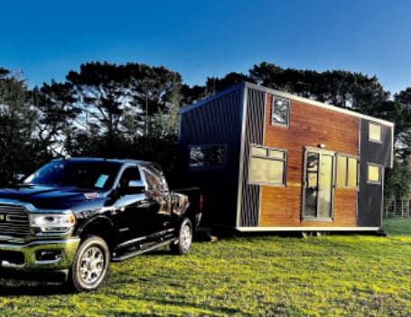 Tiny home attached to a Ford truck being towed in a paddock with trees in the background