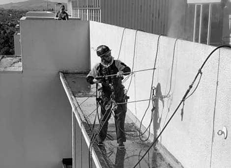 Commercial abseiler standing on the edge of a building's facade using a power washer to clean the building