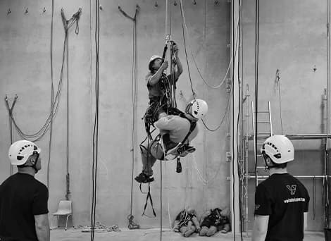 Two abseilers suspended in the air to practise and ensure health and safety as two staff members stand nearby watching