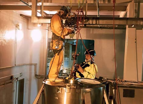 Two abseilers in their harnesses on top of a cylinder, maintaining the tank in a very confined space
