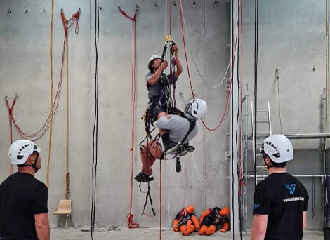 Two abseilers suspended in the air to practise and ensure health and safety as two staff members stand nearby watching