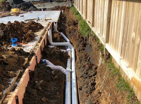 Residential drains laid underground next to a newly made house foundation on a site prepared by A1 Bobcats & Concrete