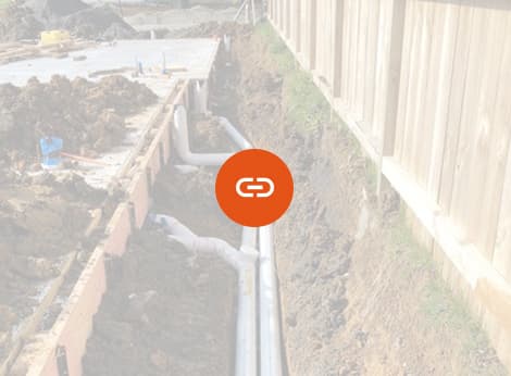 Residential drains laid underground next to a newly made house foundation on a site prepared by A1 Bobcats & Concrete