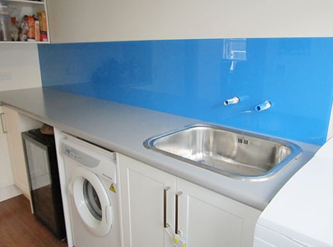 Small laundry room with a grey benchtop and royal blue reflective splashback