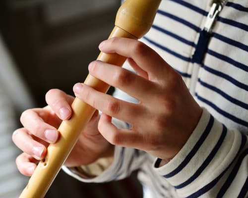 Music student playing a light wood coloured recorder with all but one holes covered 