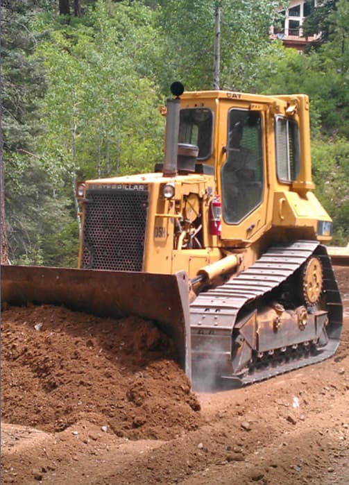 Small yellow levelling machinery being operated by an ABC Landscapes team member, pushing a pile of dirt out of the way to level the site