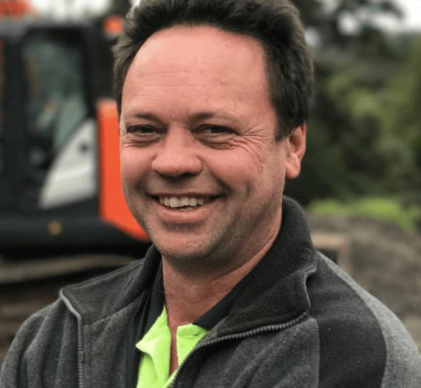 ABC Excavation & Landscapes founder William Degenkolbe smiling with an orange and white digger behind him