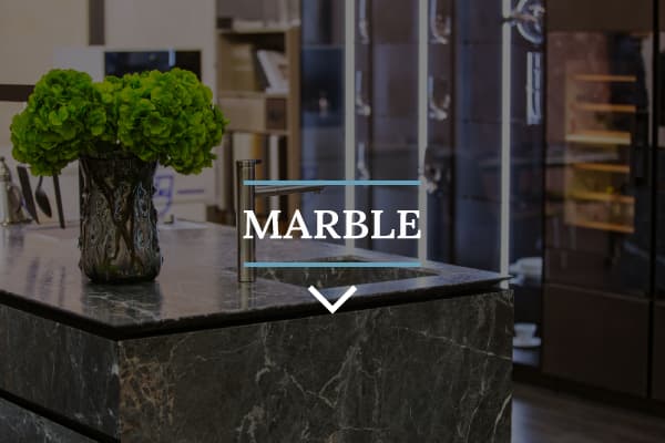 Dark marble benchtop on a kitchen island with sleek silver fixtures and a bushy green plant with modern light strips in the background