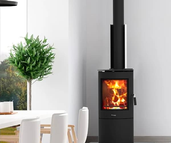 Minimalist white dining area with a tall green plant and slim free-standing black fireplace