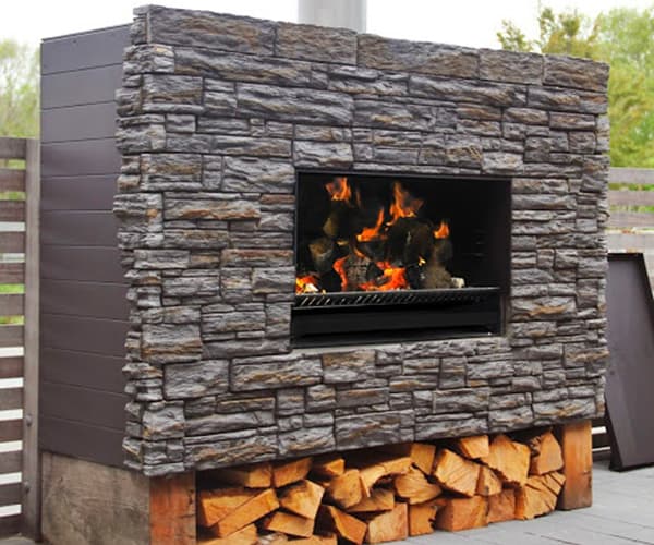 Outdoor fireplace that sits in rectangular weatherboard housing with a stone front and firewood stored below