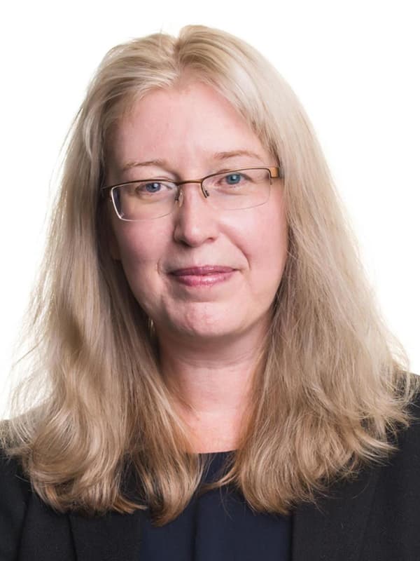 Margaret van Schaik in a blue top with a black blazer in front of a bright white wall