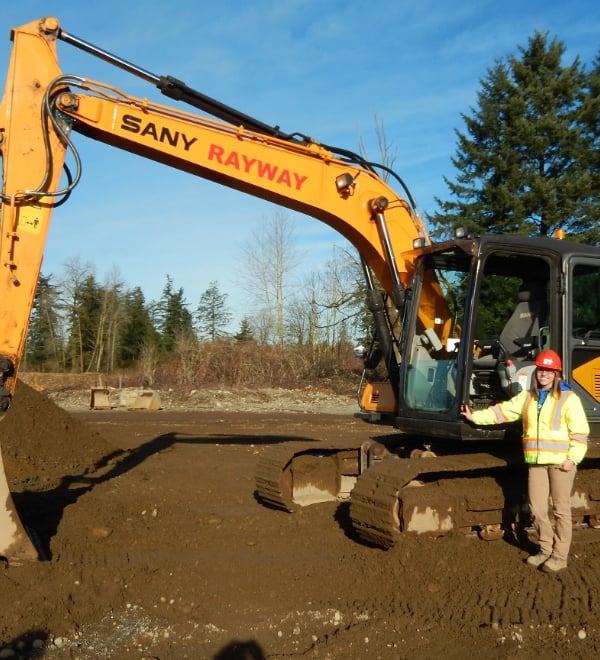ABC Excavations and landscapes worker standing next to a big yellow digger with its bucket on the ground