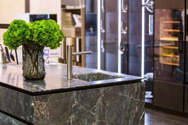 Dark marble benchtop on a kitchen island with sleek silver fixtures and a bushy green plant with modern light strips in the background
