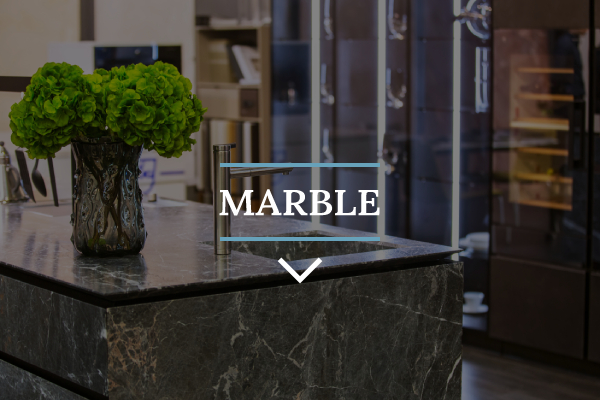 Dark marble benchtop on a kitchen island with sleek silver fixtures and a bushy green plant with modern light strips in the background