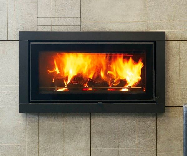 Beige stone tiled wall with an aluminum-framed built-in fireplace that displays fiery stones