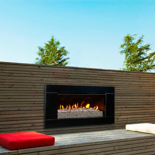 Black-framed gas fireplace built into an outdoor wooden wall next to sitting area with red and white cushions