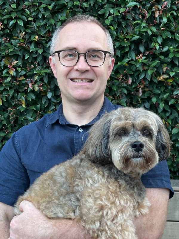Chris Bargery holding a fluffy old brown dog in front of a green hedge