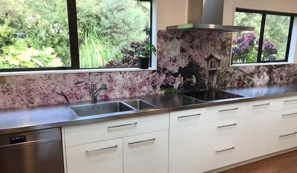 Modern white kitchen with a silver benchtop and a purple and white flowery image on the splashback