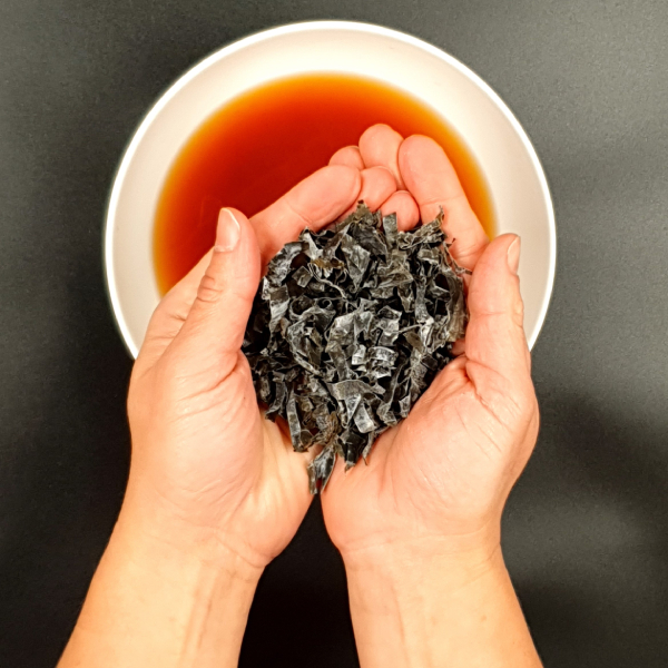 Someone using both hands to hold shredded Wakame Seaweed above a bowl