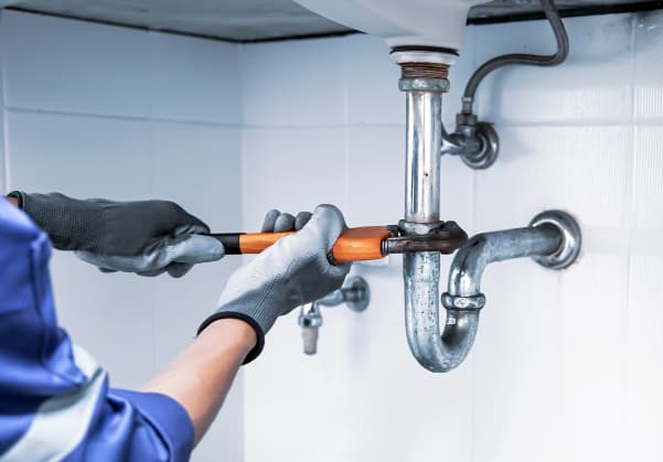 Plumber with safety gloves using a wrench to loosen a pipe below the sink 