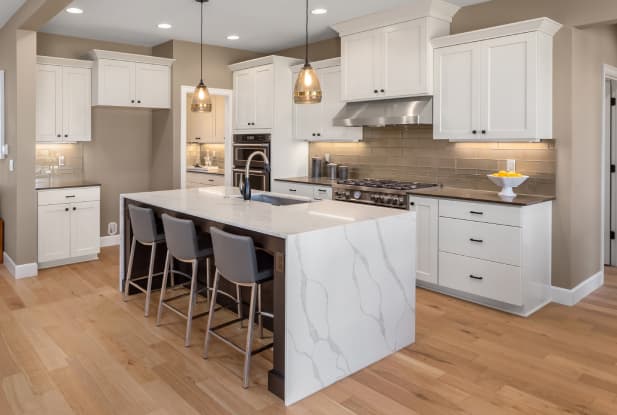 White marble waterfall benchtop on a kitchen island with grey bar chairs and a island sink, all acting as a focal point for the classic white kitchen