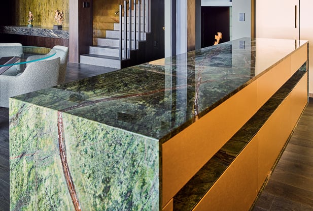 Long Kitchen island with a Green and blue nature-like benchtop with orange wood cabinets