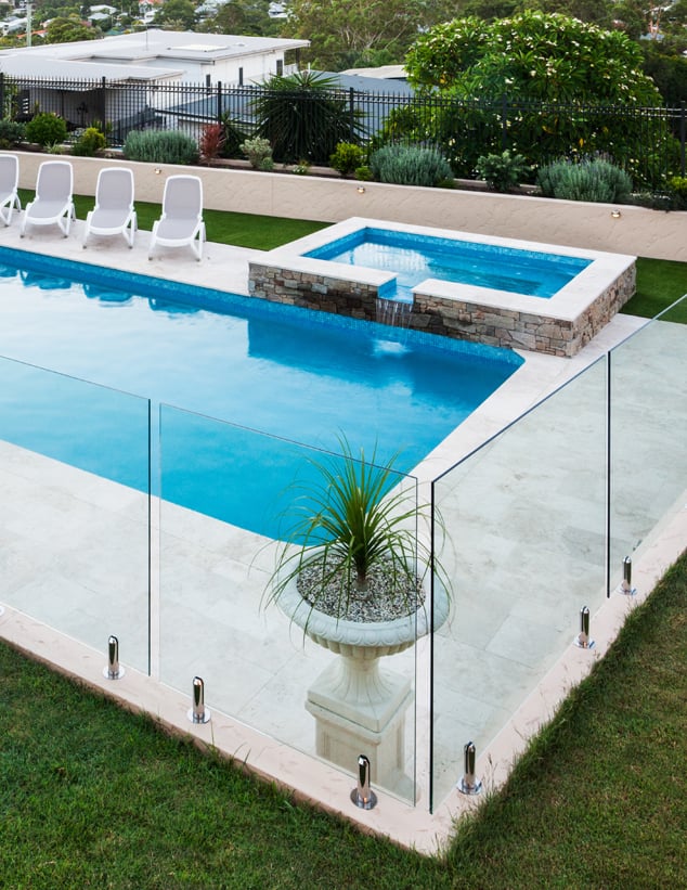 Large pool area with a white stone footpath, three grey pool chairs, and an elevated jacuzzi with water flowing into the pool