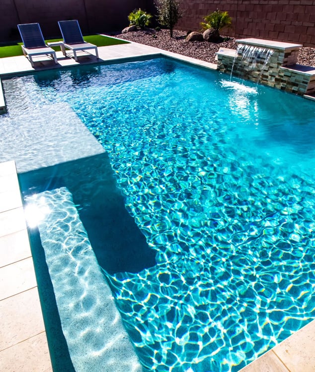Crystal blue reflective pool water with a small poolside stone fountain creating a constant flow of water