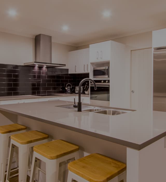 White cabinet kitchen with a black brick tile splashback and a large grey island benchtop
