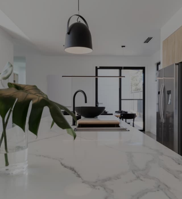 Modern white kitchen with a classy white marble benchtop, black fixtures and a monstera plant