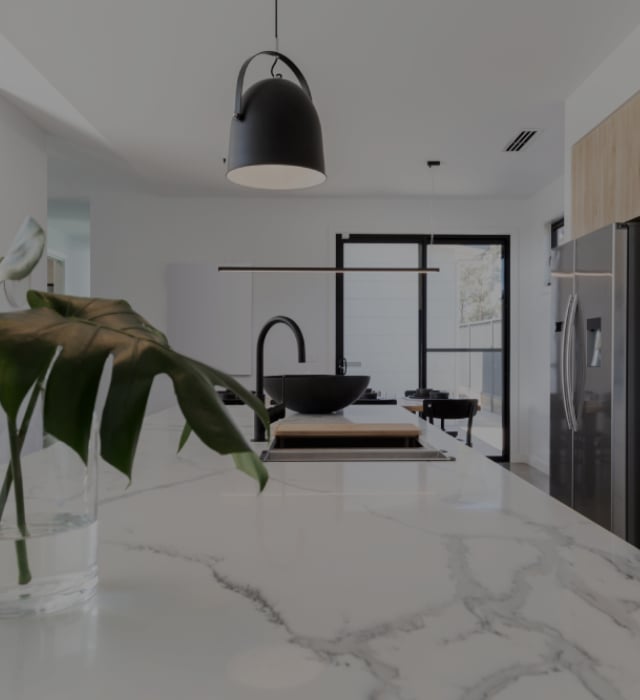 Modern white kitchen with a classy white marble benchtop, black fixtures and a monstera plant