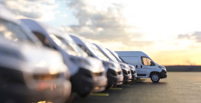 Fleet of large white work vans in a parking lot while the sun sets