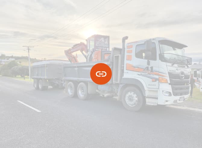 White and orange A1 Bobcats & Concrete truck with two carriages parked on the side of the road transporting an orange digger