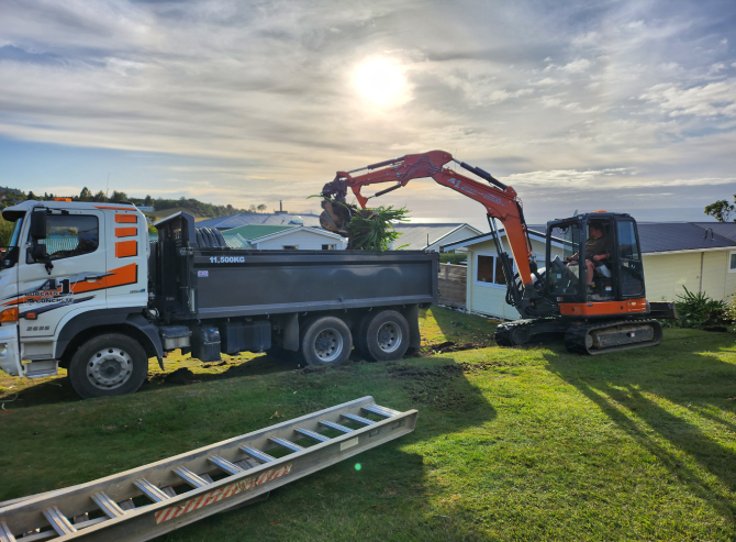 Hired orange earthmoving digger unloading plant debris from a site they're preparing for building foundations