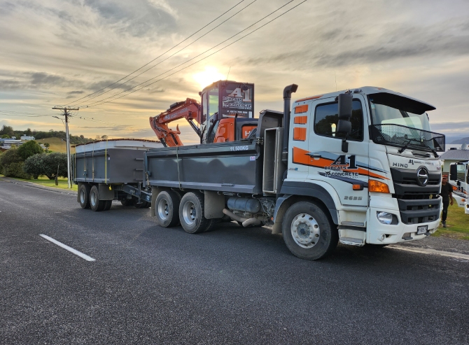 White and orange A1 Bobcats & Concrete truck with two carriages parked on the side of the road transporting an orange digger