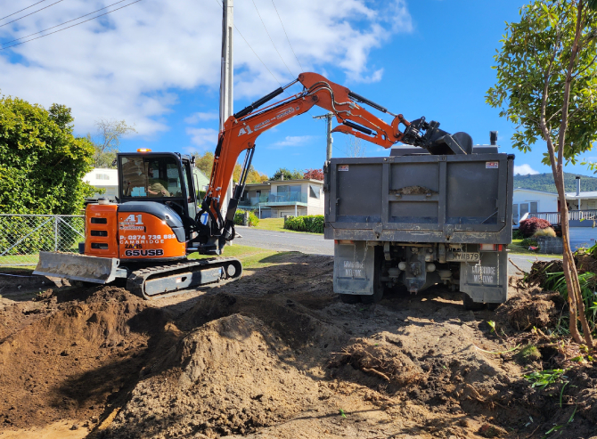 Orange earthmoving digger unloading dirt from a site they're levelling and making ready for building foundations