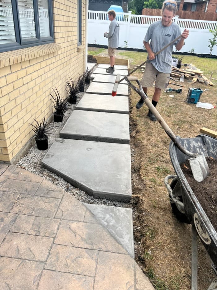 Concrete tiles being put in the ground by the York Landscaping team to then surround with dirt to make a nice path on the side of a house