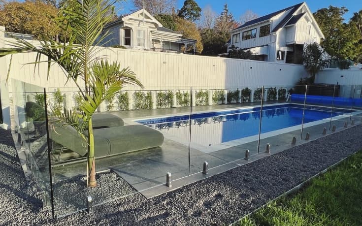 Small to medium sized pool with a concrete path surrounded by gravel and divided by a modern glass fence