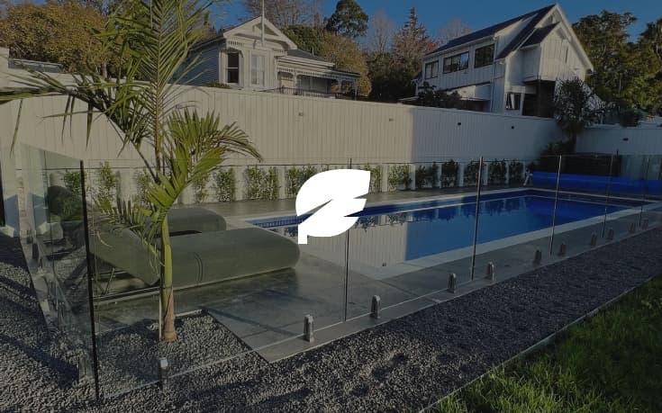 Small to medium sized pool with a concrete path surrounded by gravel and divided by a modern glass fence