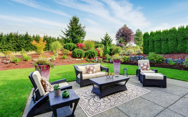 Vibrant and comfortable outdoor sitting area with flowery plants and trees in the distance that surround the whole property