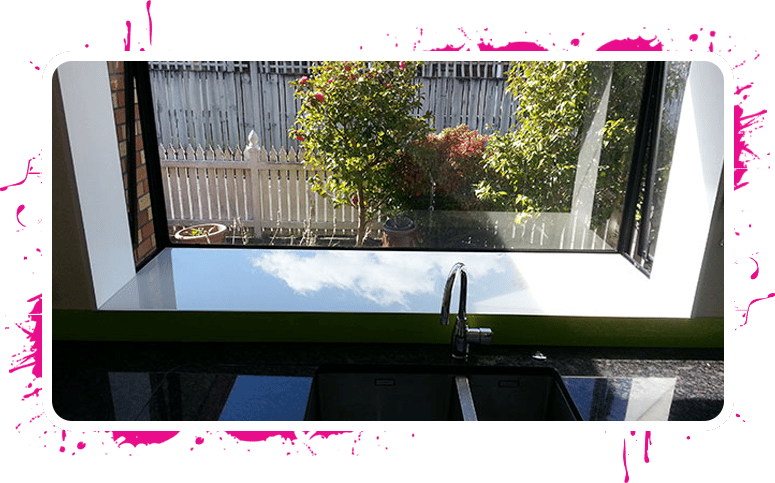 Custom made green splashback above a kitchen sink and a large window that looks out to a small garden and fence line 