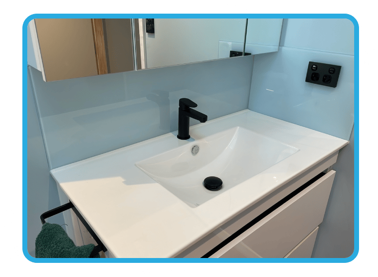Old white basin with an unbuilt sink and a large white tile splashback covering the wall up to below the mirror and window