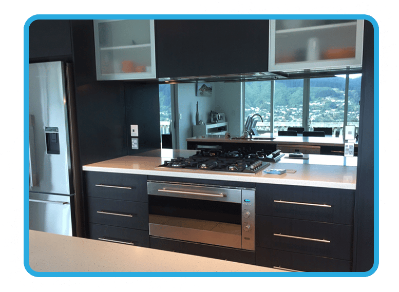 Kitchen with black cabinets and a white stone benchtop with the reflection of the dining room shown in the mirror splashback