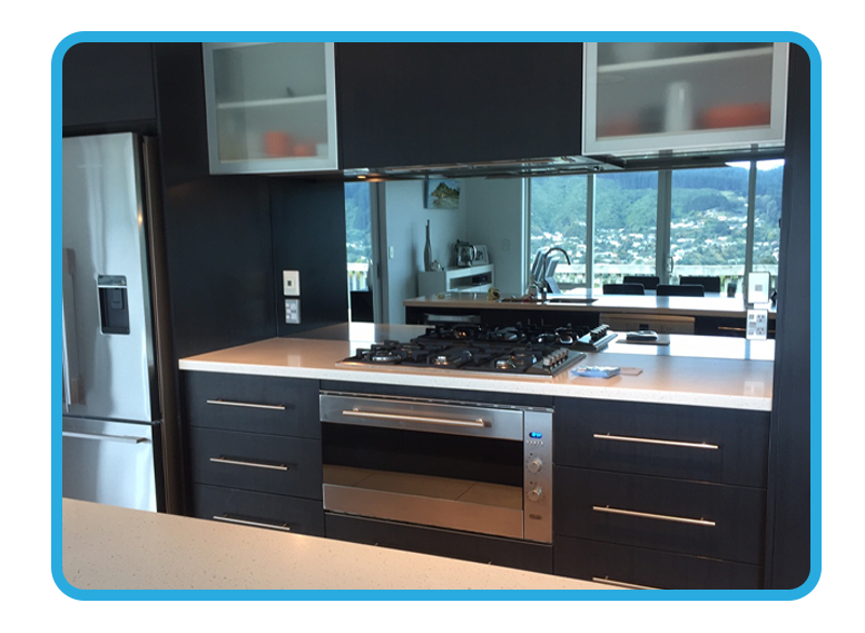 Kitchen with black cabinets and a white stone benchtop with the reflection of the dining room shown in the mirror splashback