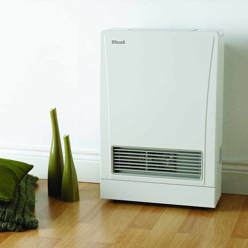Wooden floor and a white wall with green ornaments and pillows next to a new white energysaver heater